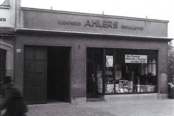 Das Ahlers-Geschäft hat eine einladende Fassade mit großen Fenstern, die die Vielfalt der angebotenen Waren präsentieren.