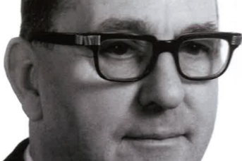 In einem formellen Outfit präsentiert sich ein Mann mittleren Alters mit Brille, der in die Kamera blickt und gelassen wirkt.