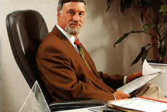 In einem eleganten Büro sitzt ein Mann mit grauen Haaren und Bart, der aufmerksam auf seine Papiere schaut und entspannt wirkt.